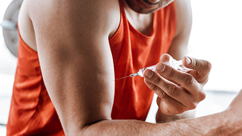A muscular man at a gym giving himself a steroid injection.