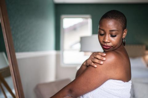 A Black woman inspects the skin on her shoulder.